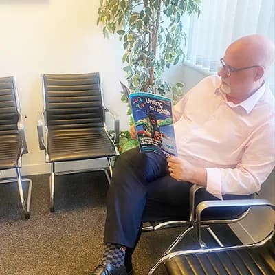 A man reading Uniting For Health in a hospital waiting room